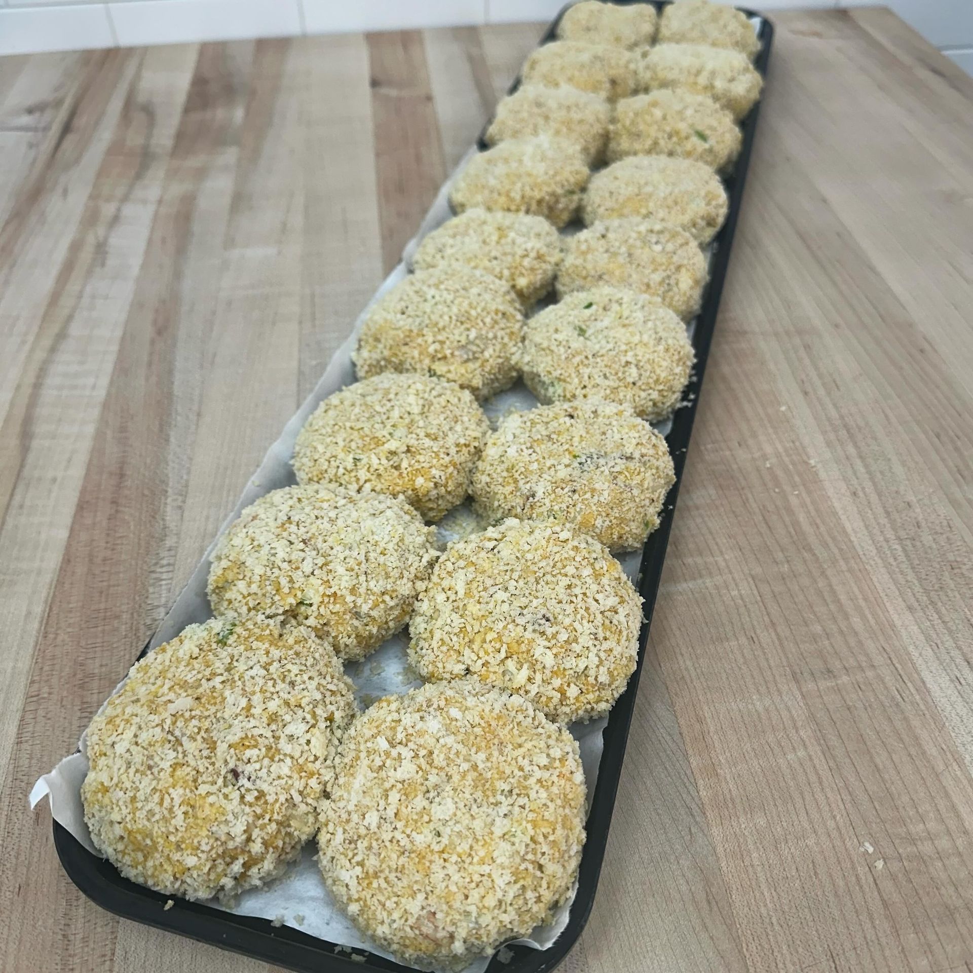 Tray of breaded, round, golden-brown patties on a wooden surface.