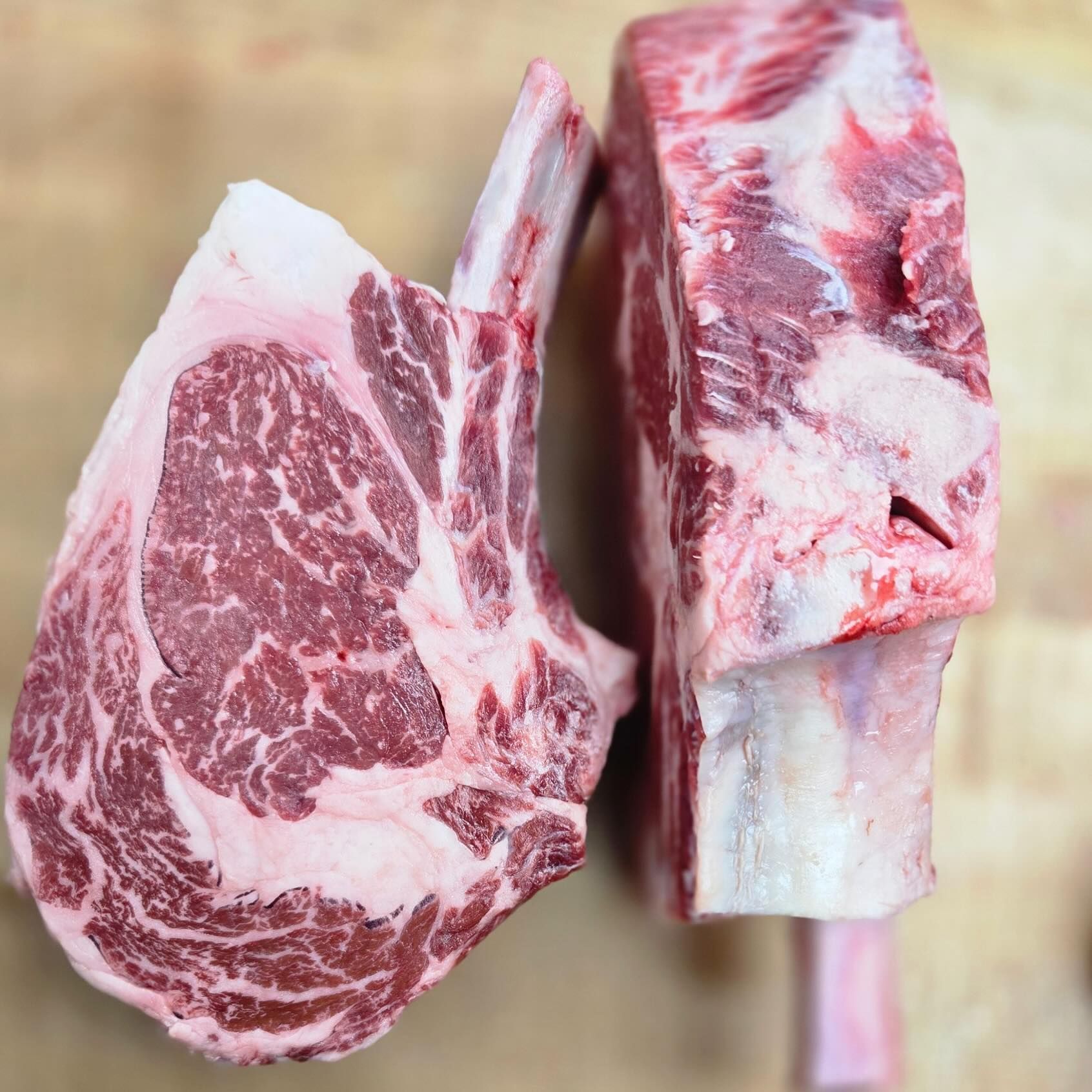 Two thick, raw, marbled ribeye steaks with large bones.