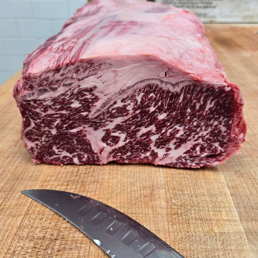 Large raw ribeye steak with heavy marbling, on a wooden cutting board, knife in front.