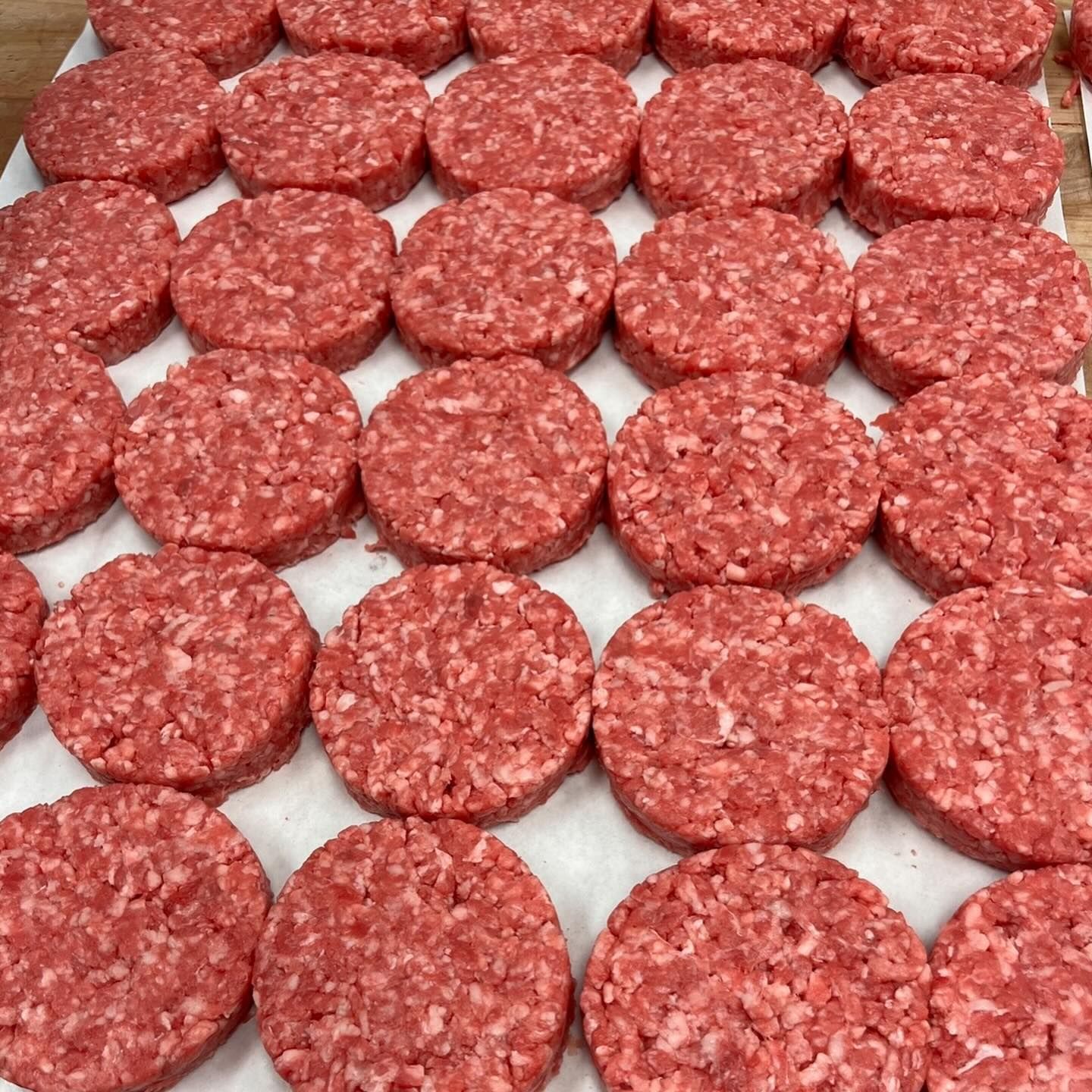 Raw, round hamburger patties arranged in rows on a white surface.