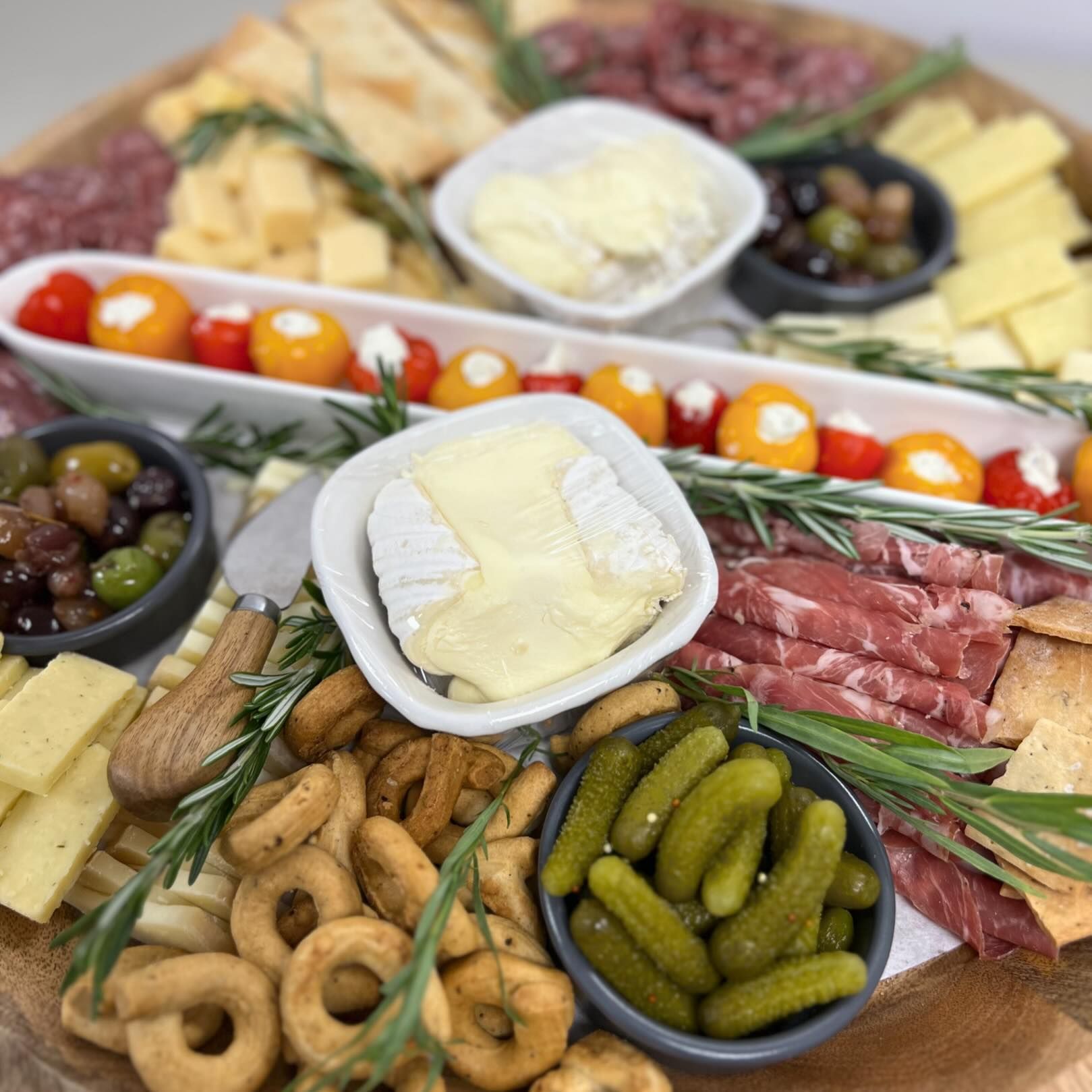 Charcuterie board with cheese, meats, olives, pickles, tomatoes, and crackers.
