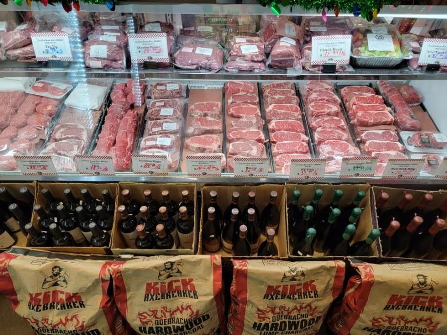 Meat display case at a butcher shop with various cuts of meat. Charcoal and bottles of beer are displayed below.