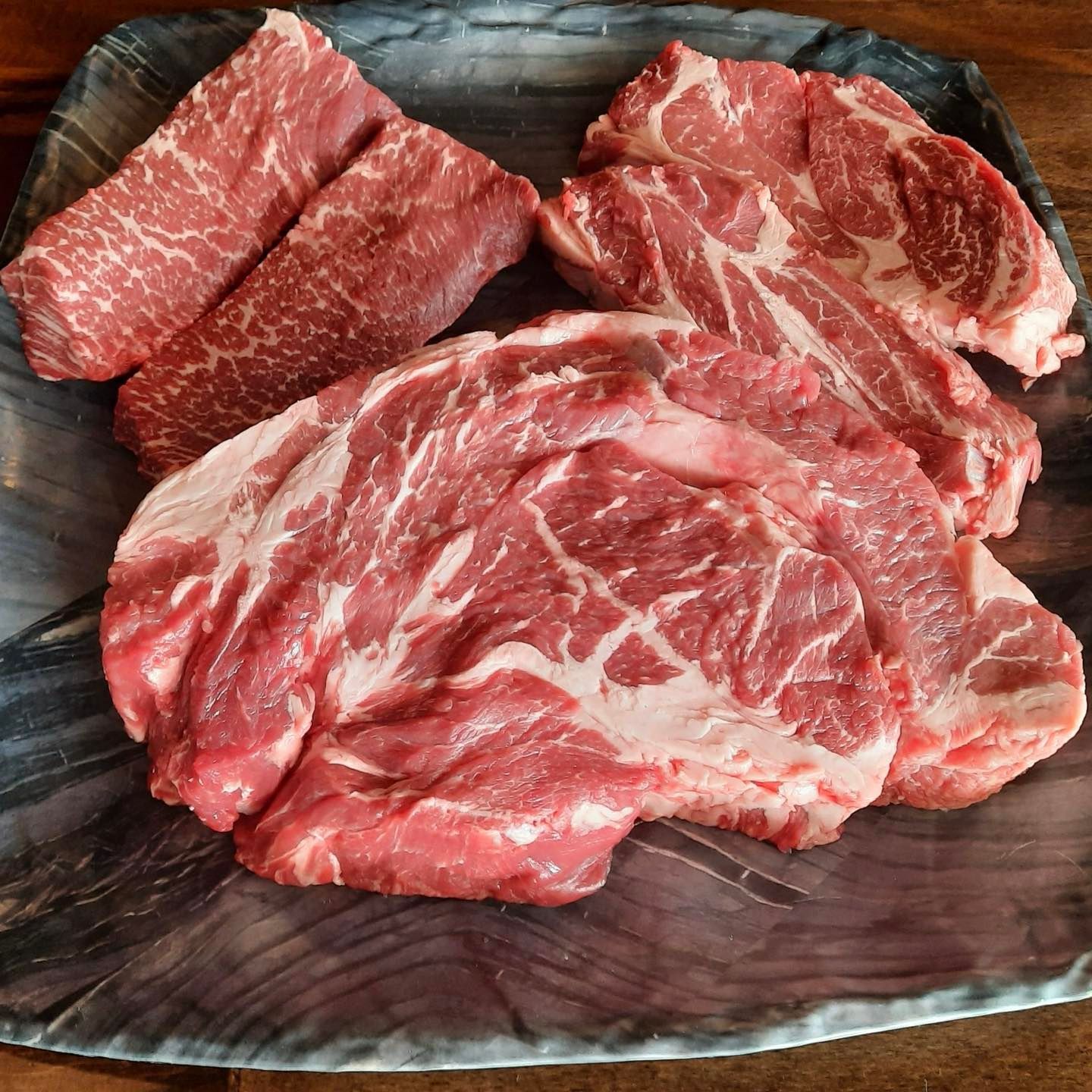 Raw cuts of marbled meat on a gray speckled plate.