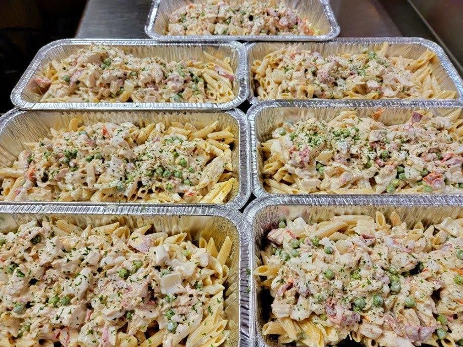 Aluminum foil trays filled with penne pasta, creamy sauce, and herbs.