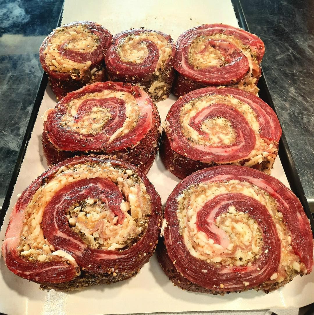 Close-up of raw, spiral-cut beef rolls stuffed with a light-colored filling, arranged on parchment paper in a pan.
