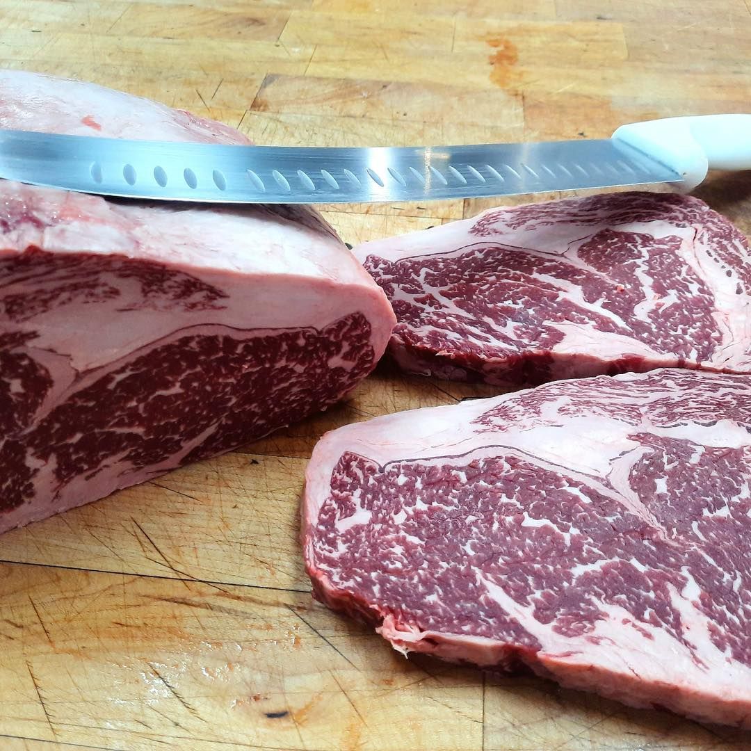 Raw steaks on a wooden surface, with a carving knife resting on one of the cuts.