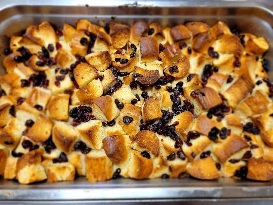 Bread pudding in a metal baking pan, topped with dark berries.