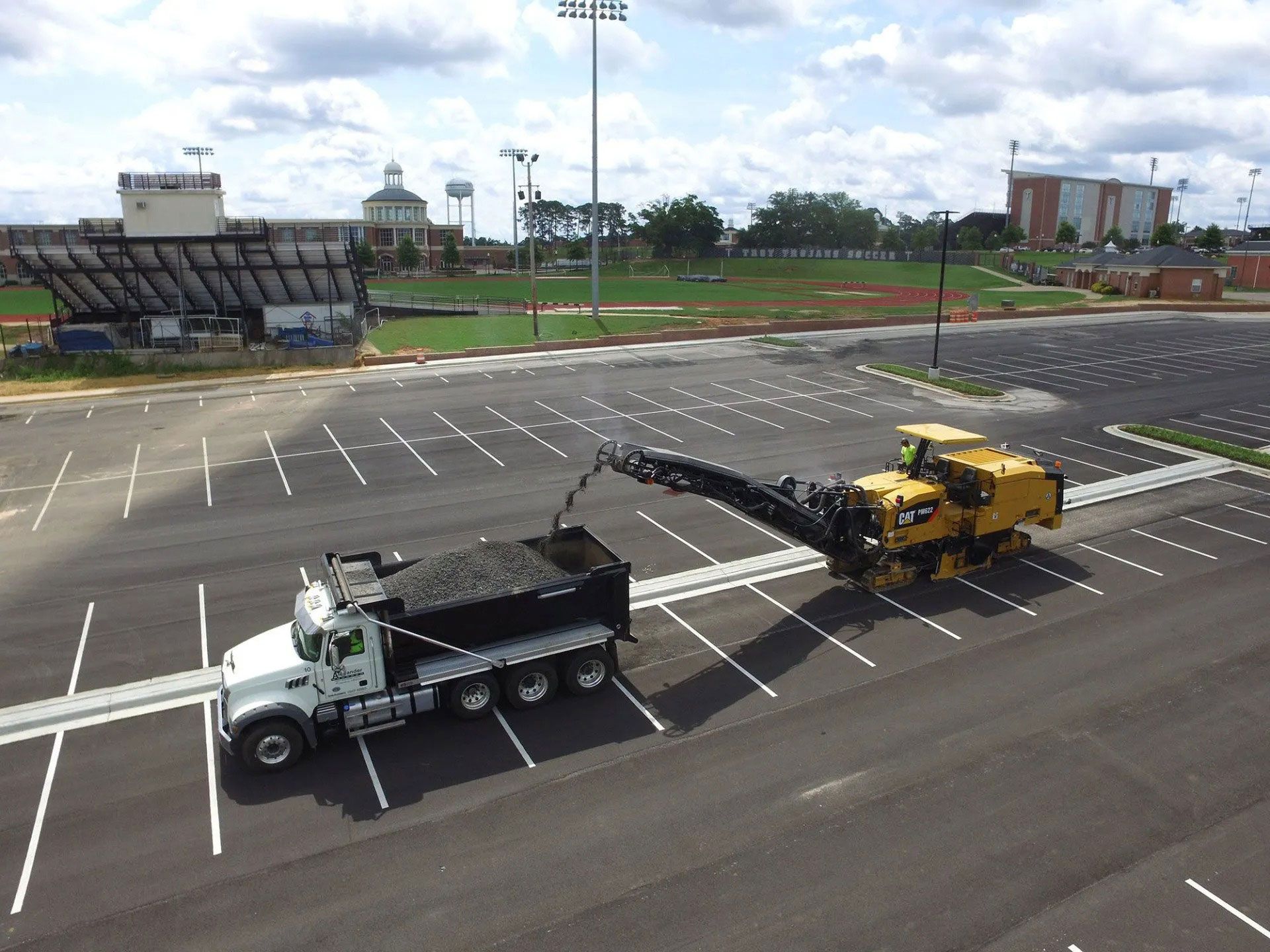 Two tow trucks in an empty parking lot, one white and one yellow, with a stadium in the background