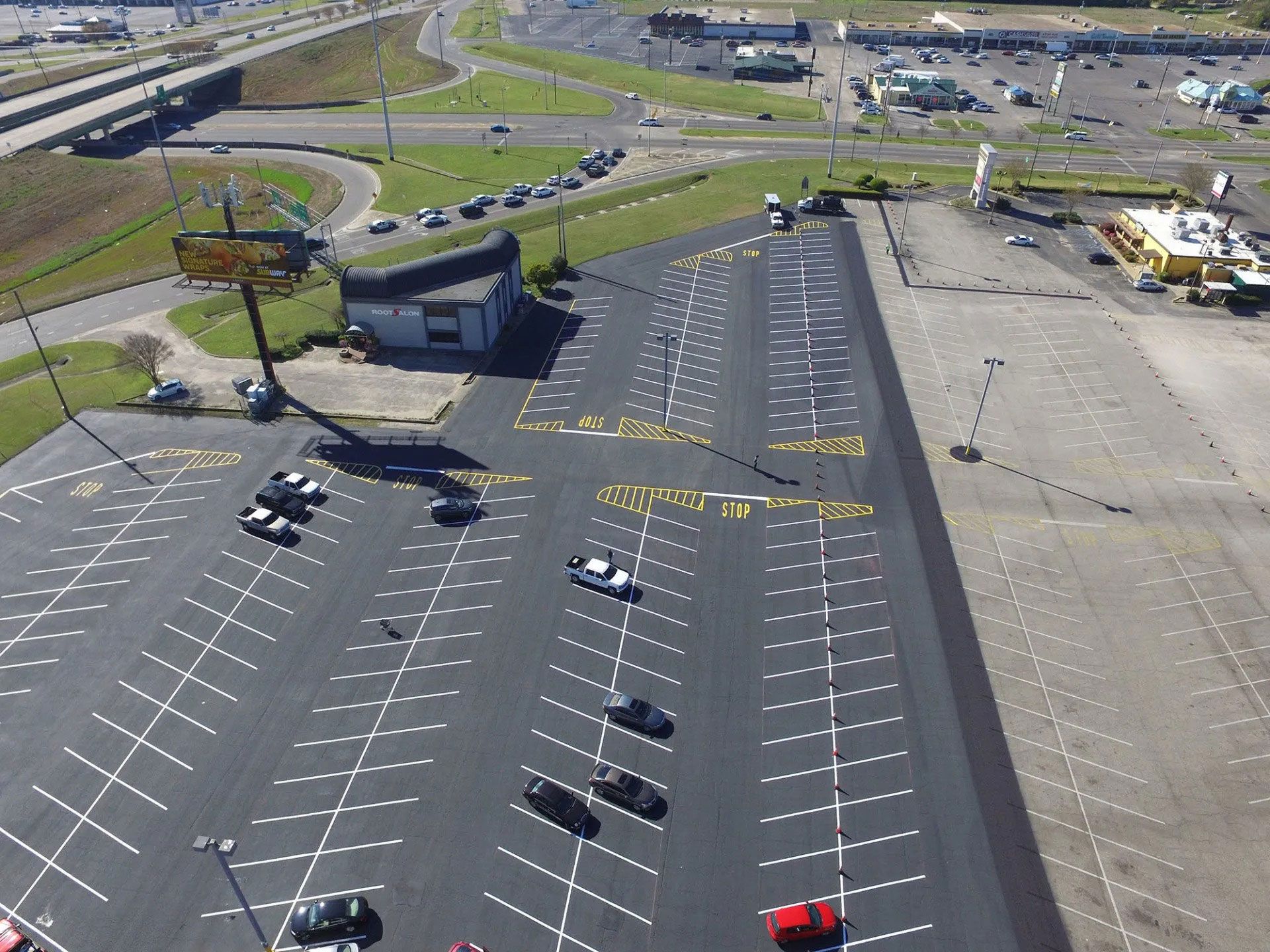 Aerial view of a mostly empty parking lot with a few cars and nearby roads