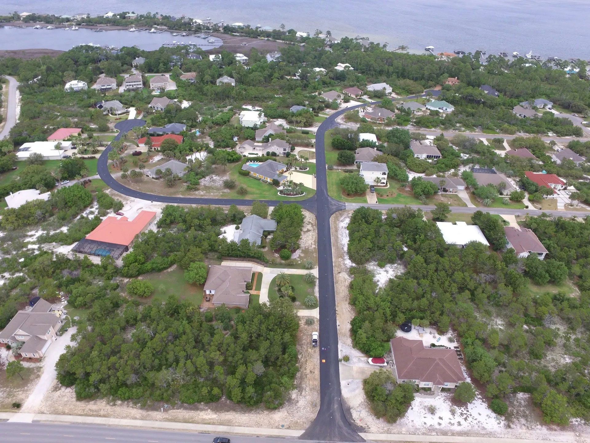 Aerial view of a coastal neighborhood with homes, roads, and dense greenery near the water.