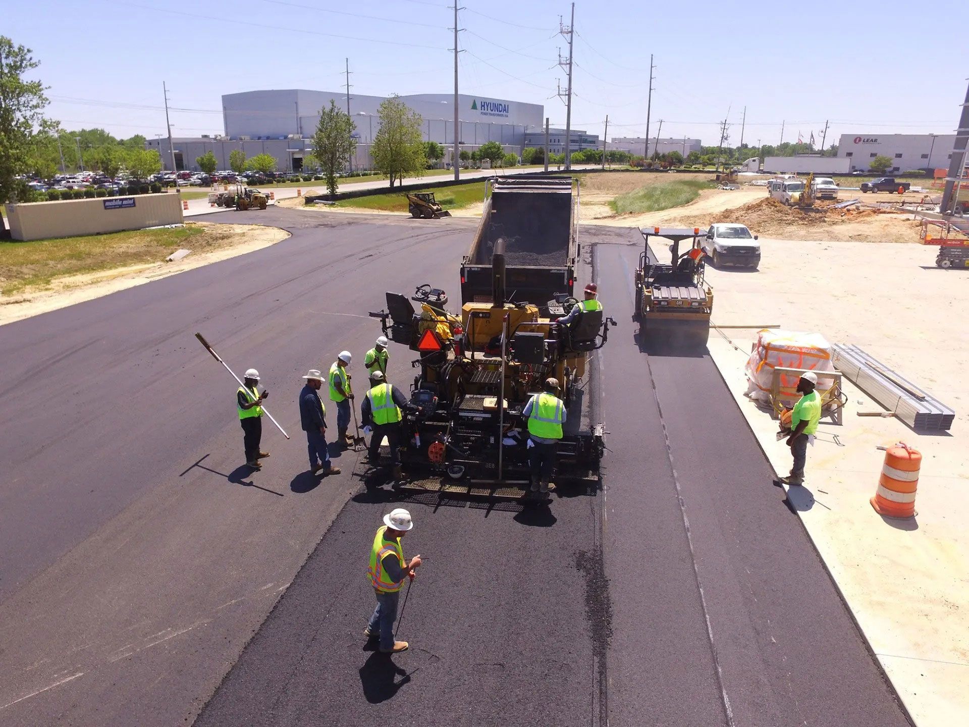 Road crew paving a new asphalt street with workers and heavy machinery under bright daylight