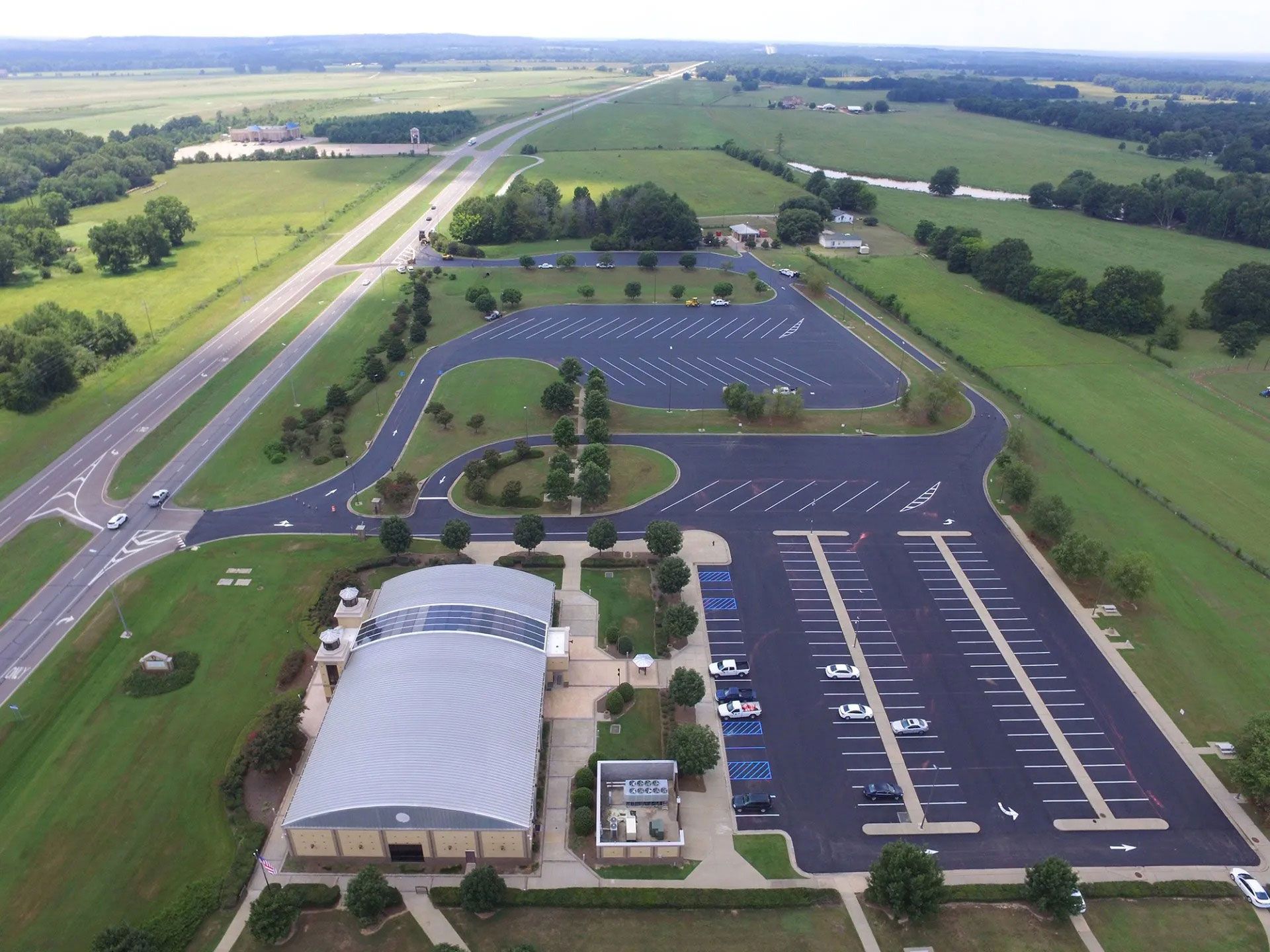 Aerial view of a large building, parking lot, and surrounding fields under a clear sky.