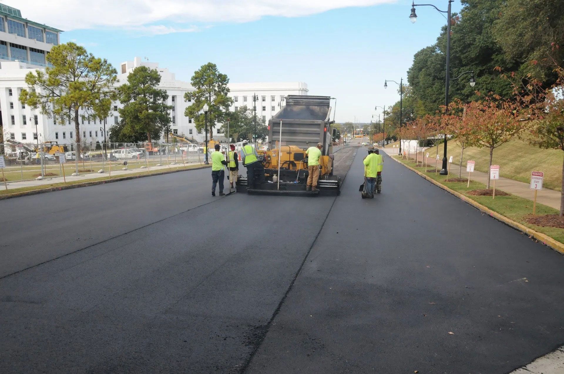 Road crew paving a wide street, with workers and equipment on fresh black asphalt in daylight