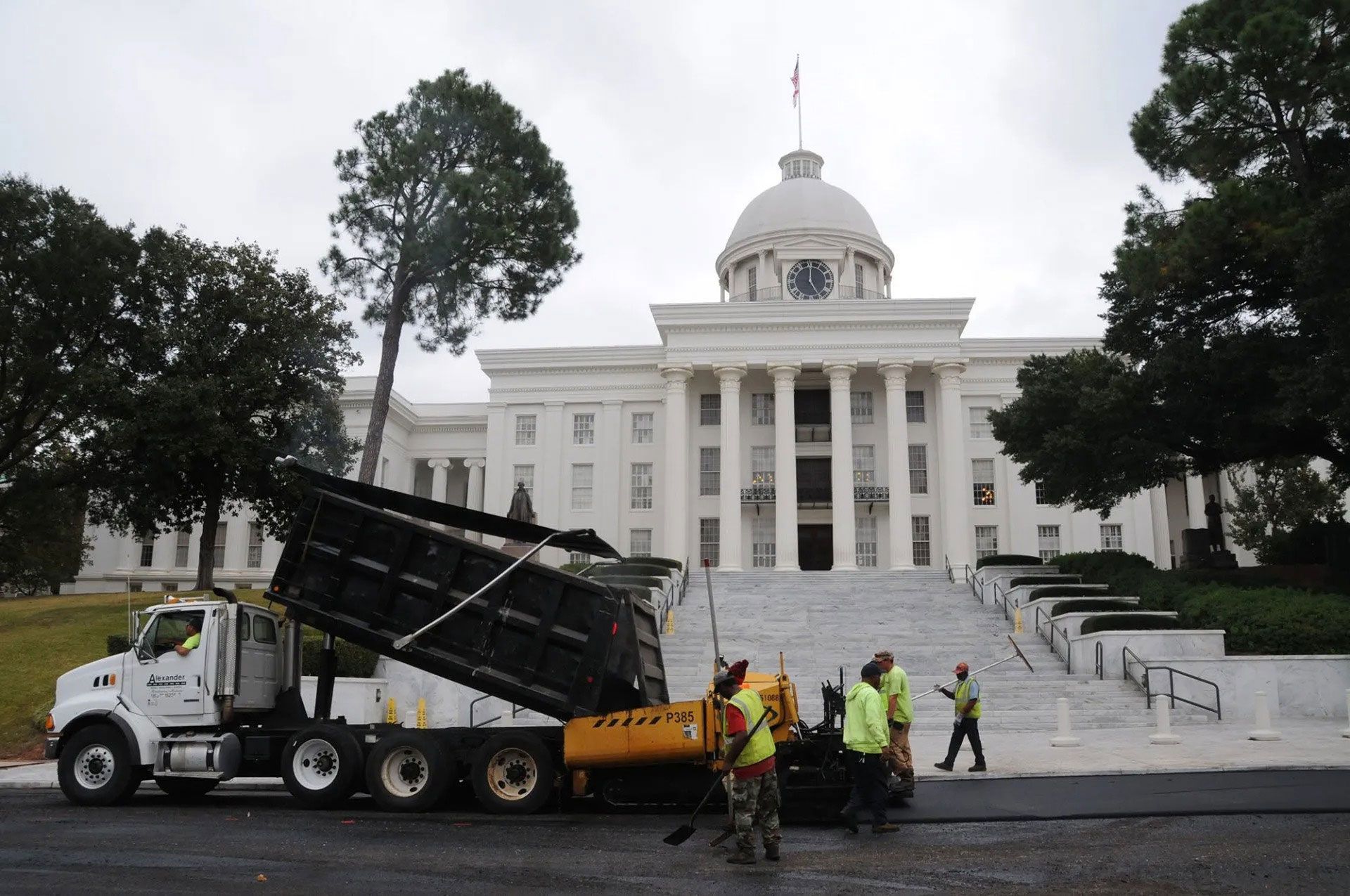 Workers and a dump truck dumping debris in front of a white domed capitol building