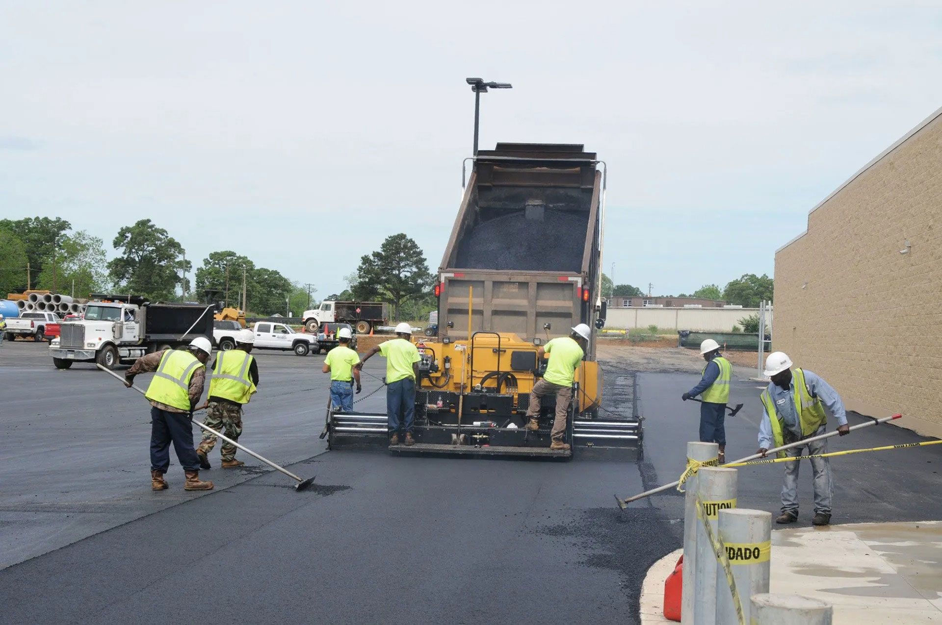 Road crew paving a street with a large asphalt machine and workers in safety vests.