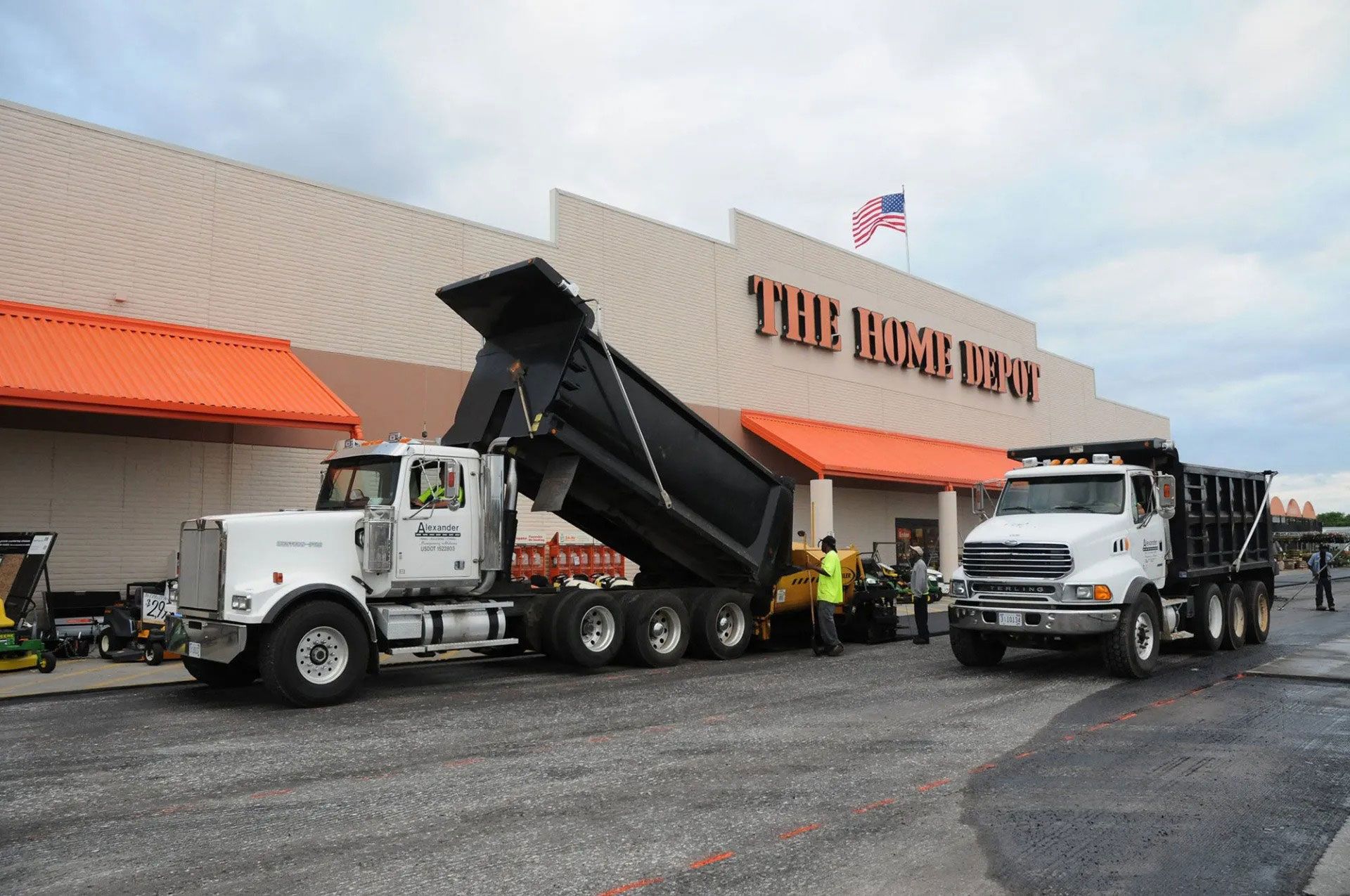 Two dump trucks parked outside The Home Depot loading gravel in the lot