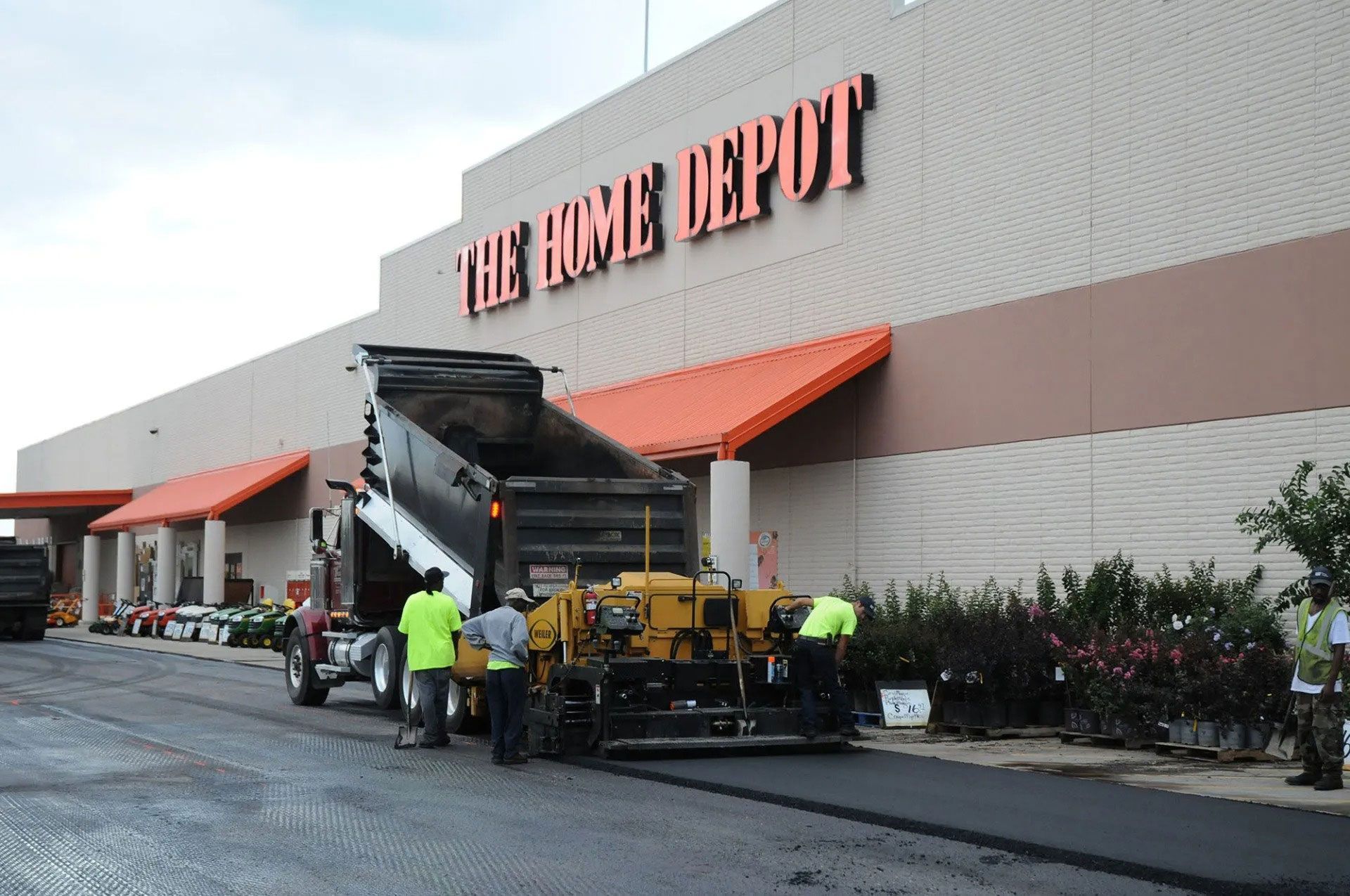Workers repaving pavement outside a Home Depot storefront with an asphalt machine