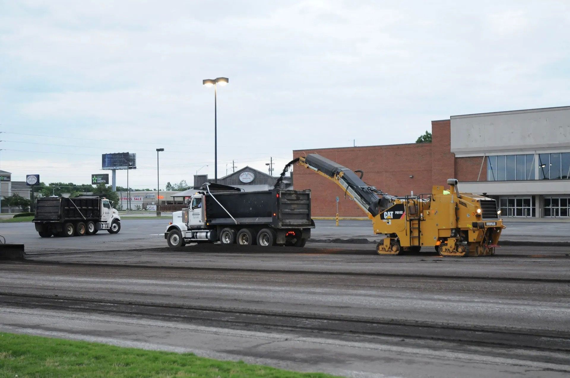 Construction equipment paving a road beside a building under an overcast sky