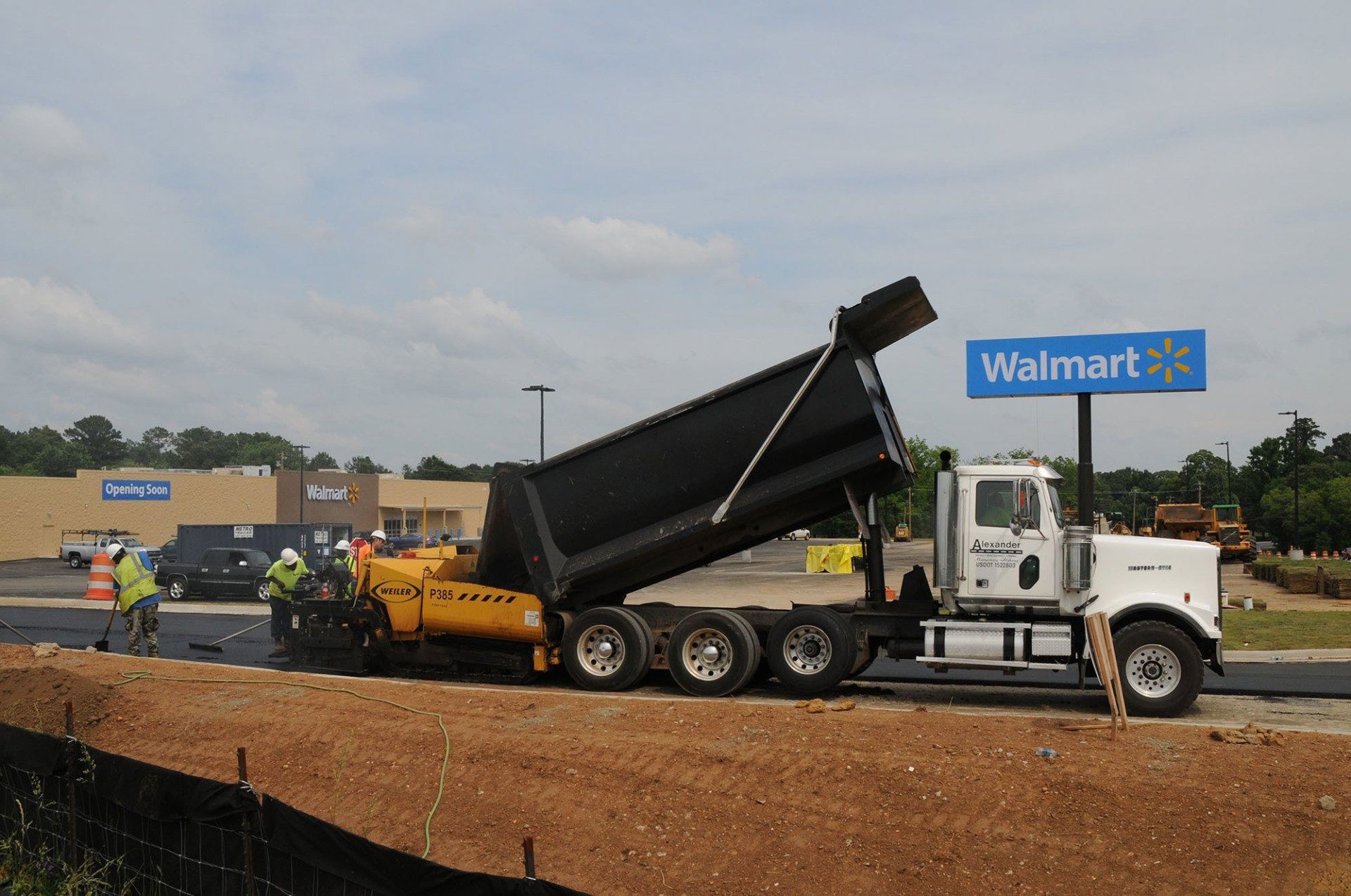 Dump truck unloading gravel at a Walmart construction site with workers nearby.