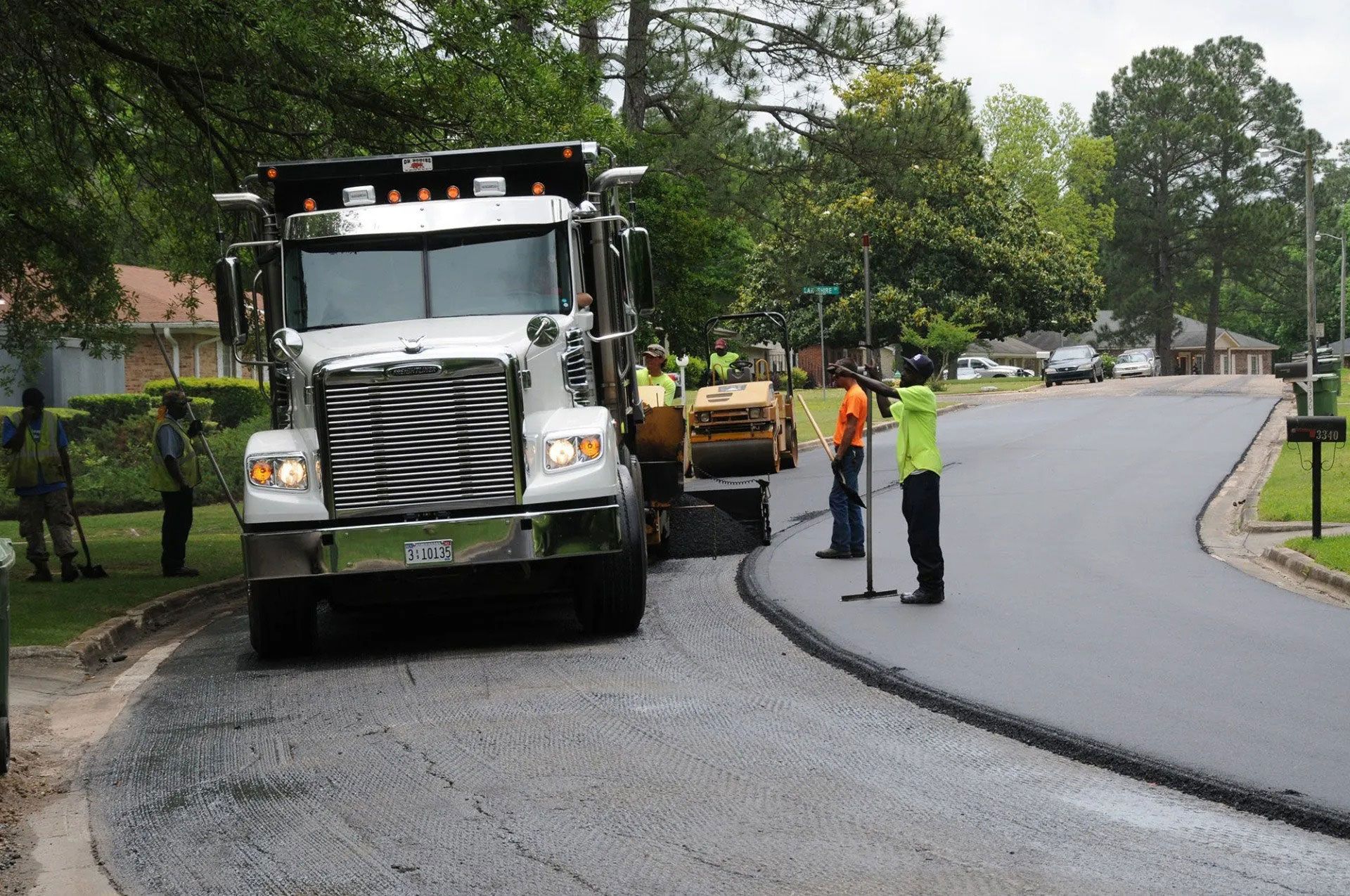 Road crew paving a curved street with a dump truck and workers on site.