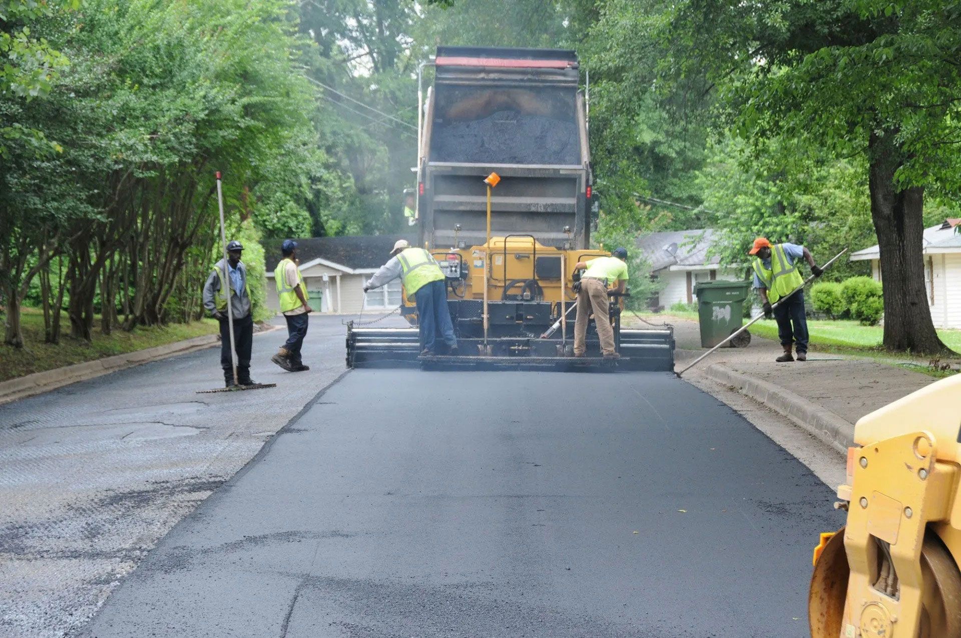Road paving crew laying fresh black asphalt on a tree-lined road