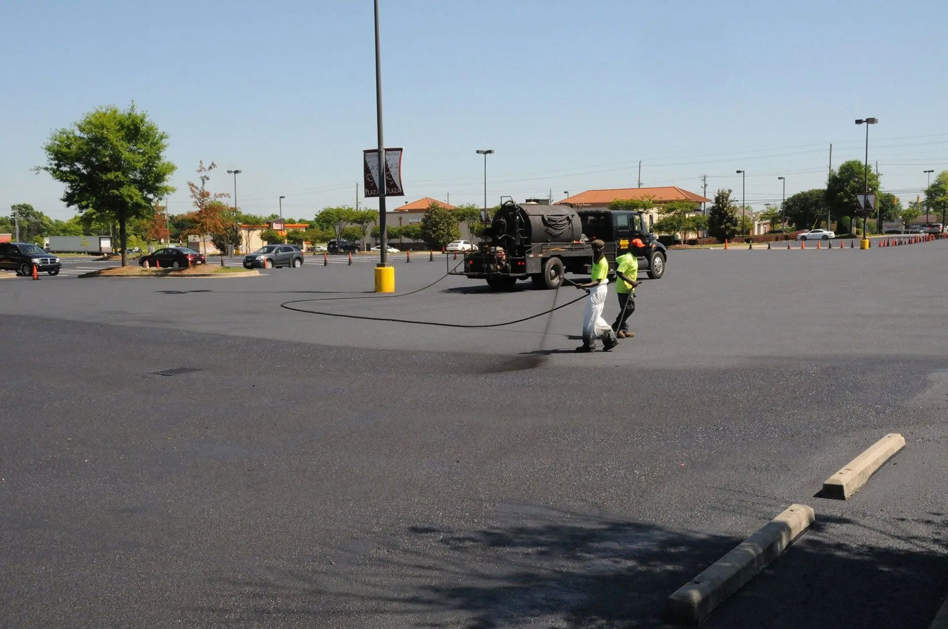 Roadside construction crew spraying asphalt in a large parking lot on a sunny day