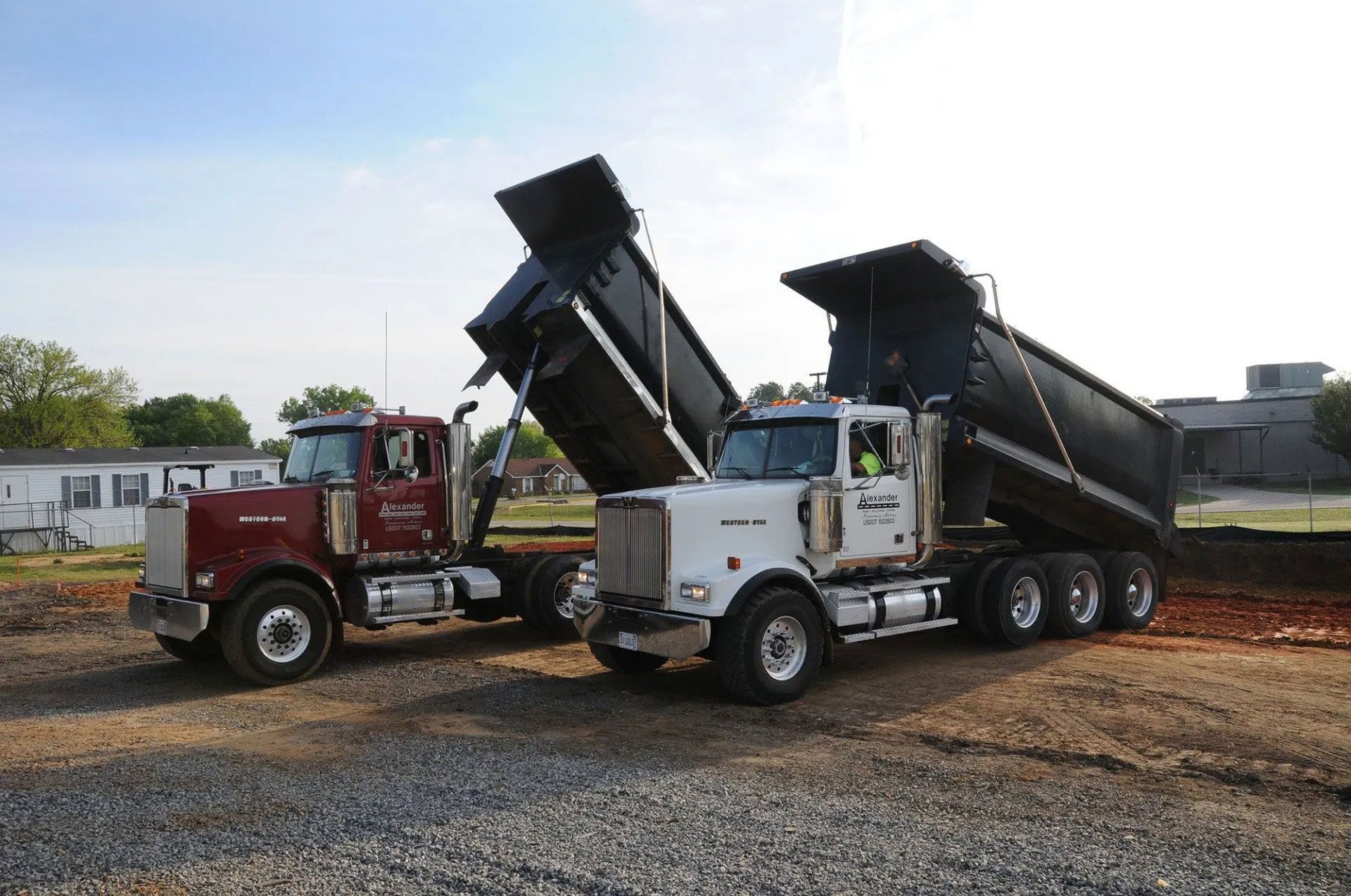 Two dump trucks with raised beds parked side by side on a gravel lot