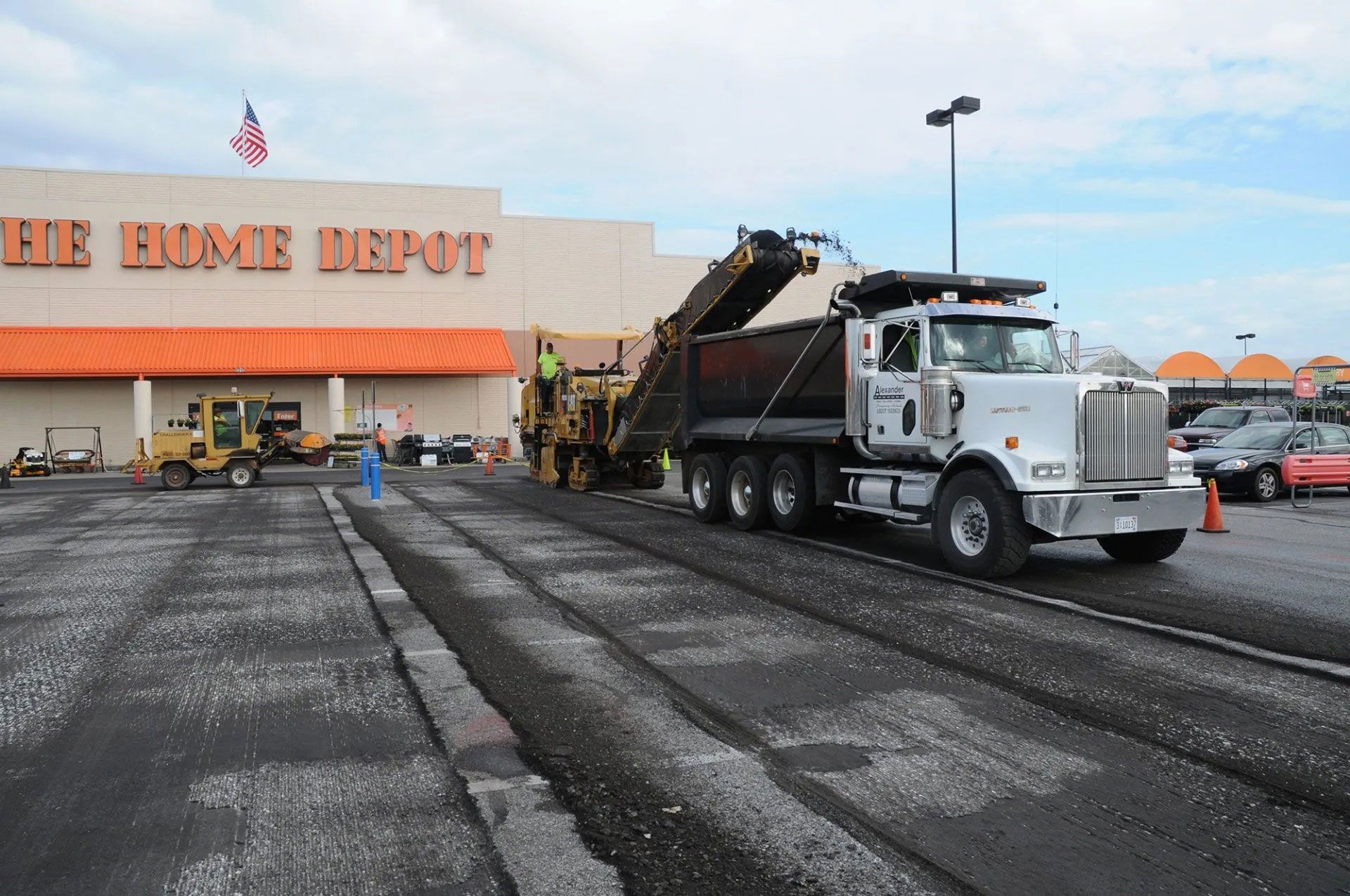 Dump truck at a Home Depot parking lot, loading asphalt near the store entrance