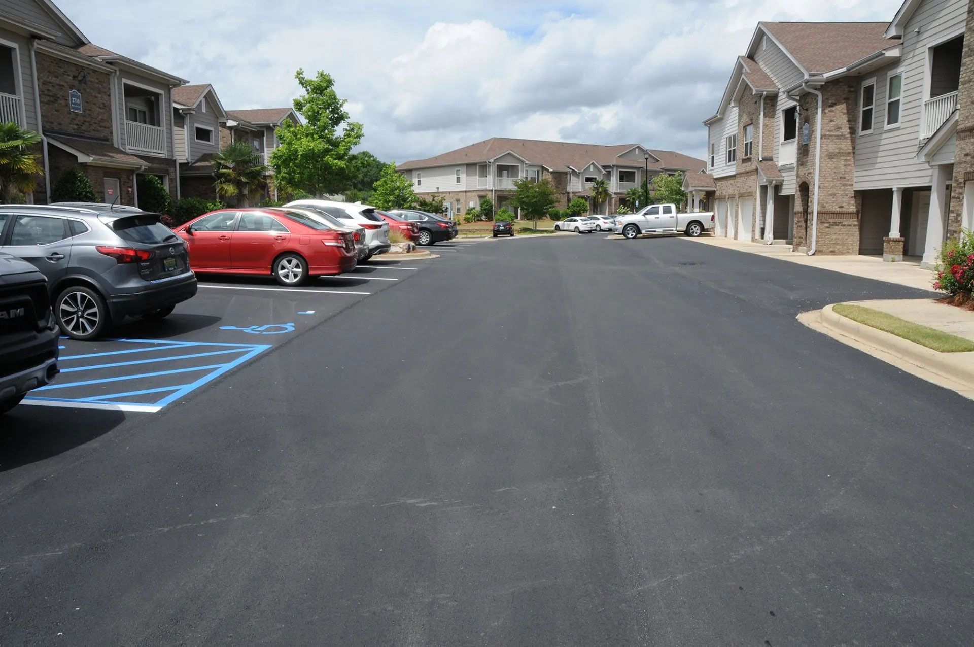 Apartment complex parking lot with parked cars and blue accessible spaces along a paved drive