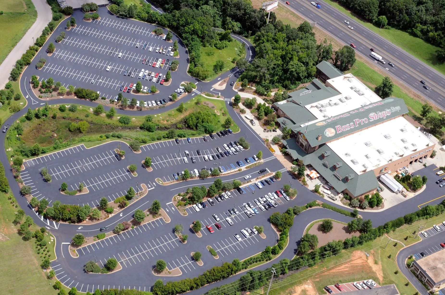 Aerial view of a large parking lot beside a white commercial building and a busy road.