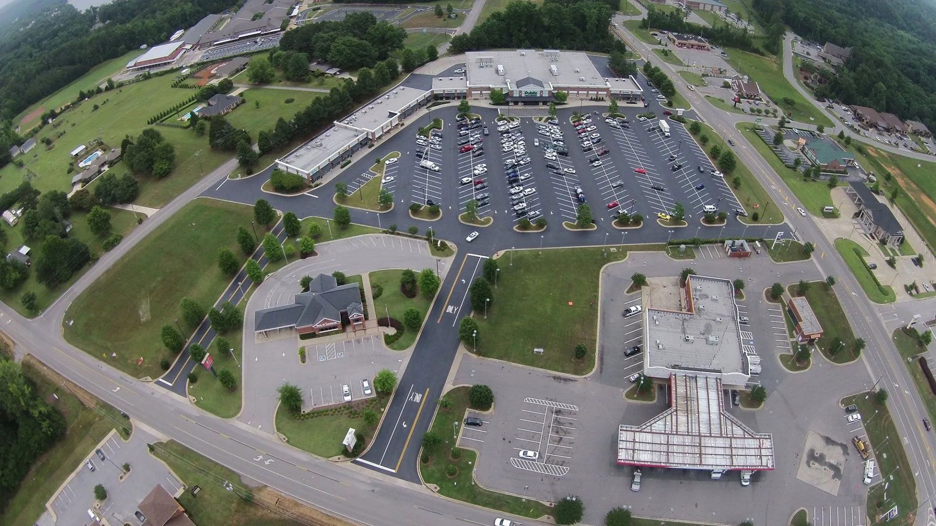 Aerial view of a large parking lot beside a commercial building and grassy grounds.