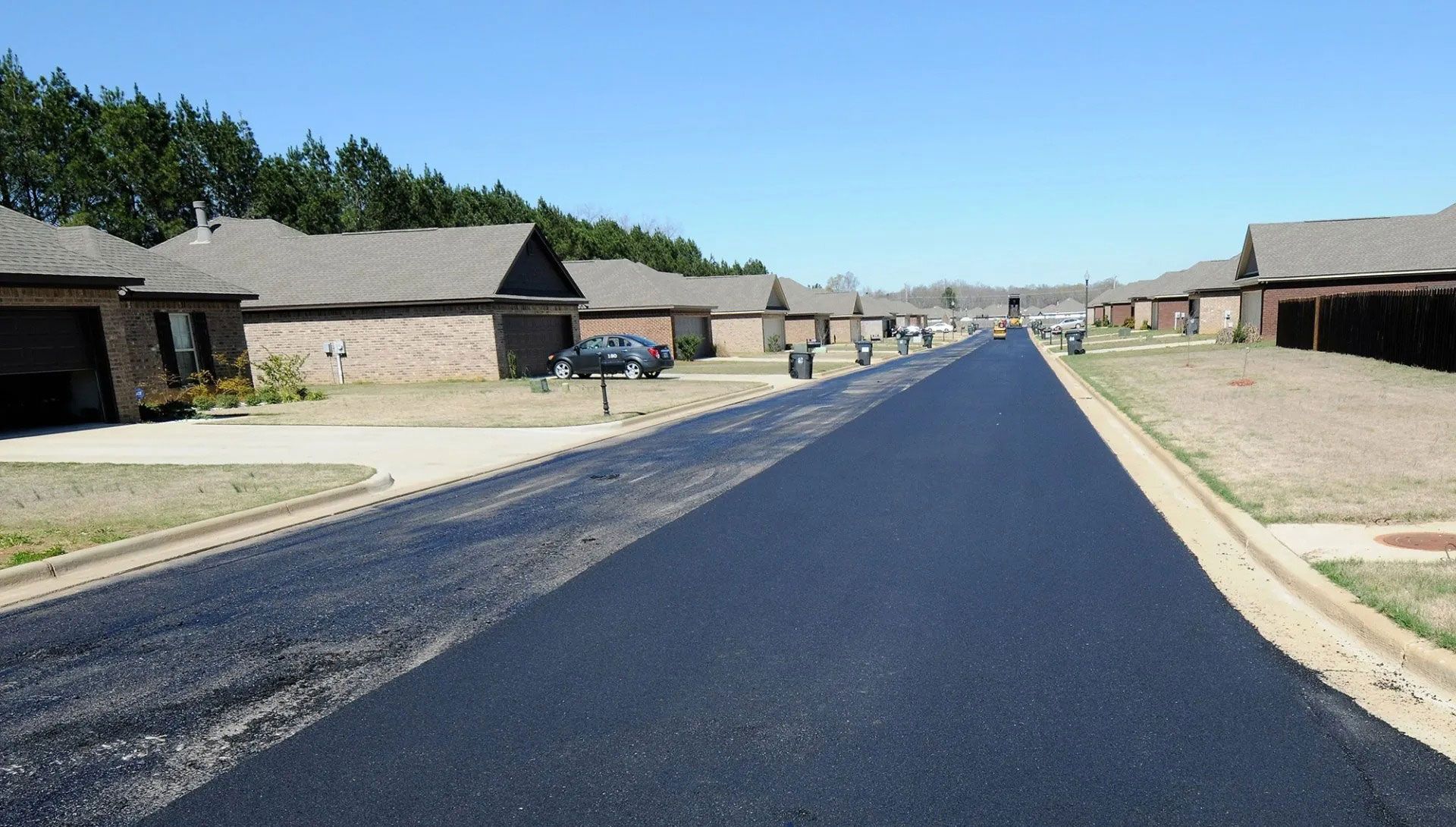 Freshly paved suburban street lined with single-story houses under a clear blue sky