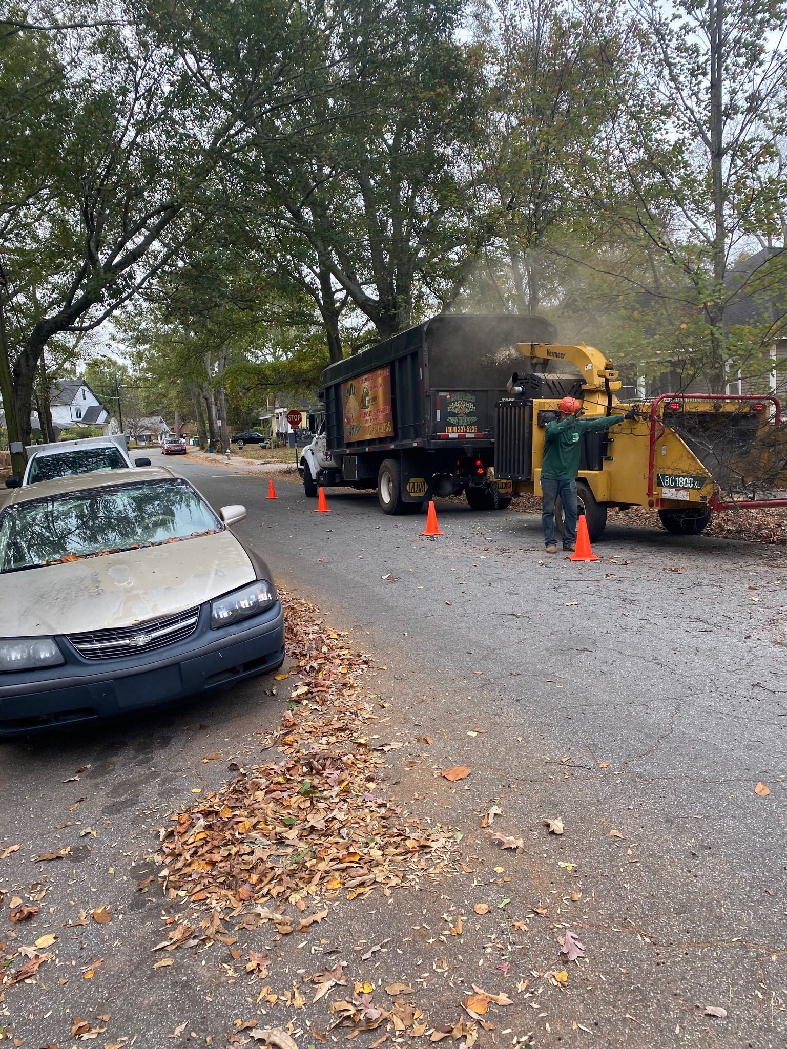 A car is parked on the side of the road next to a tree chipper.