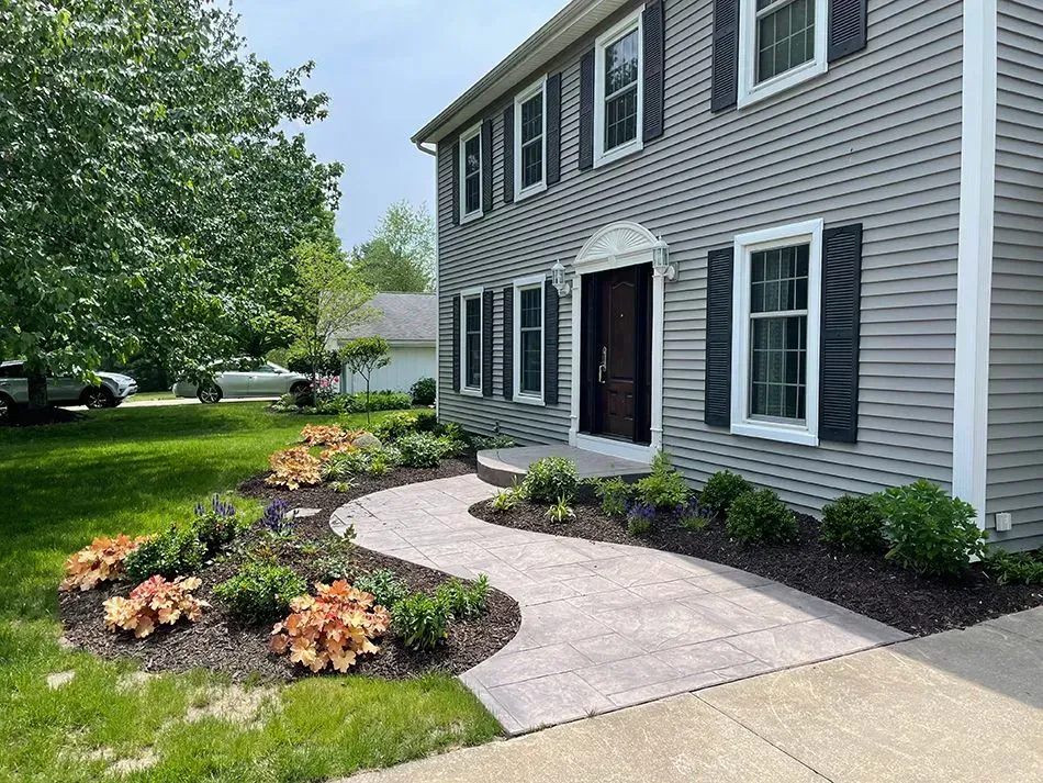 House exterior with a stone walkway, landscaped flower beds, and green lawn.