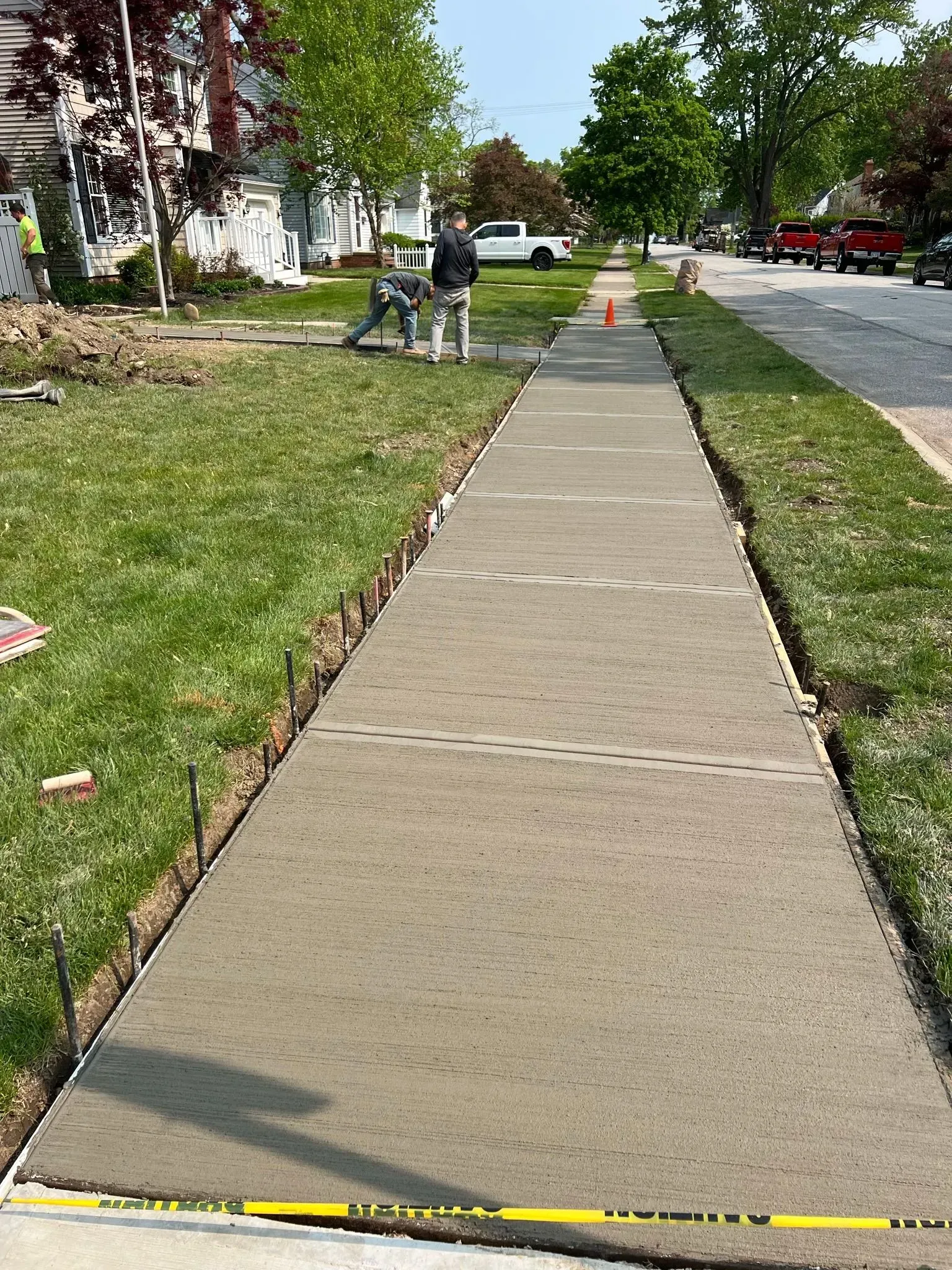 Newly poured concrete sidewalk with a worker standing nearby. Grass borders the sidewalk on both sides.