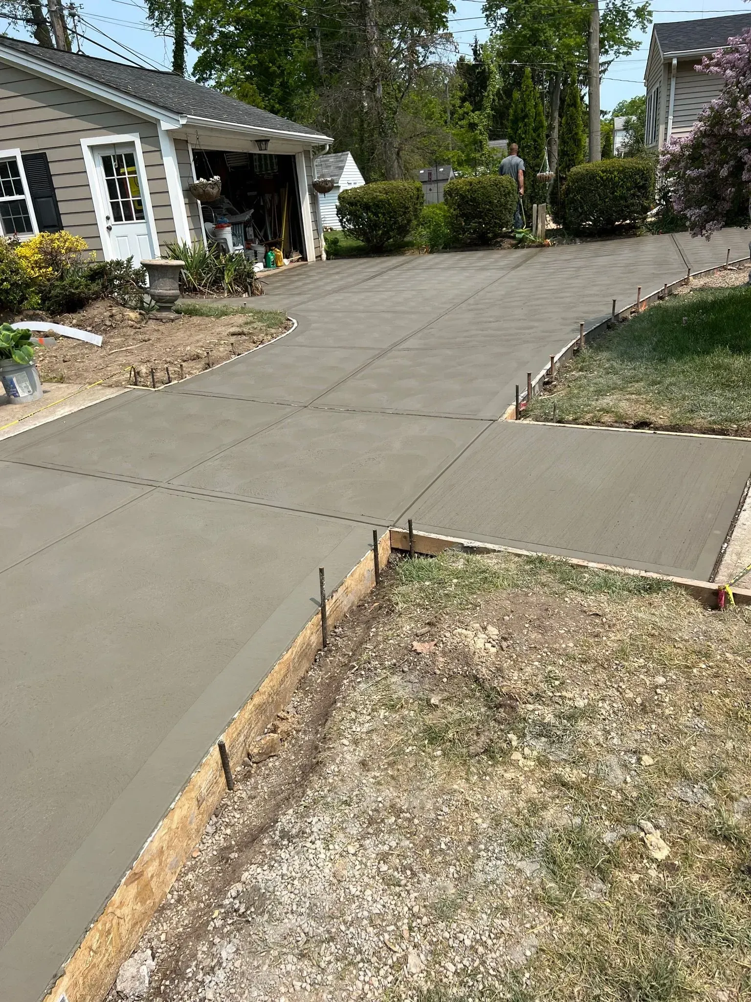 Freshly poured concrete driveway with wooden formwork and a house in the background.