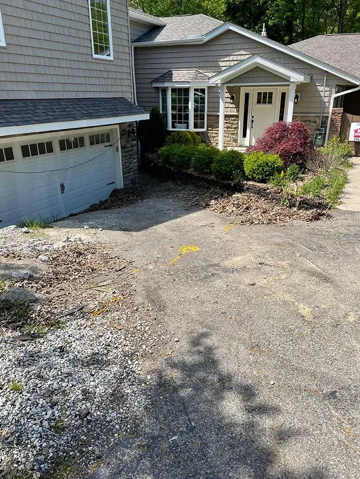 A two-story house with a driveway. The garage door is closed, and the front entrance has a door under a small roof.