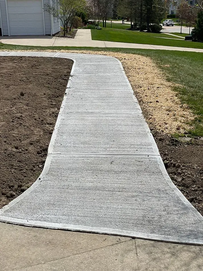 Concrete walkway leading from driveway to lawn, surrounded by dirt and grass.