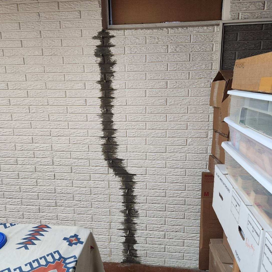 Brick wall with a long vertical crack, with boxes and a small table visible.