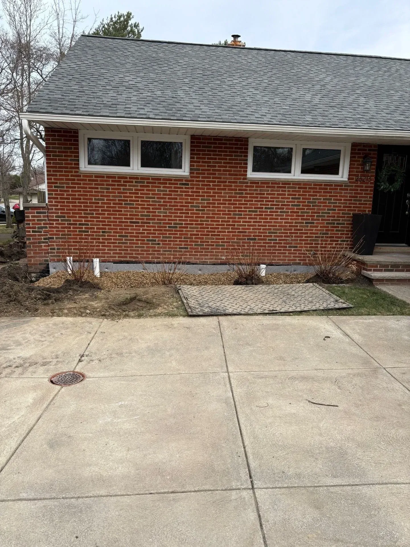 Red brick house with two windows, concrete driveway, and exposed foundation.