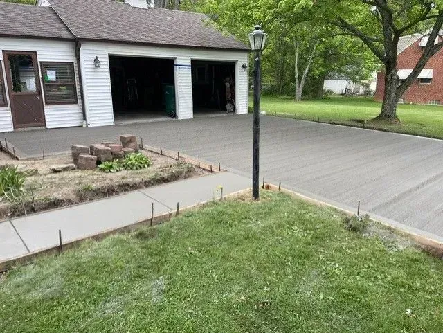 Newly poured concrete driveway and sidewalk next to a garage, grass in the foreground.