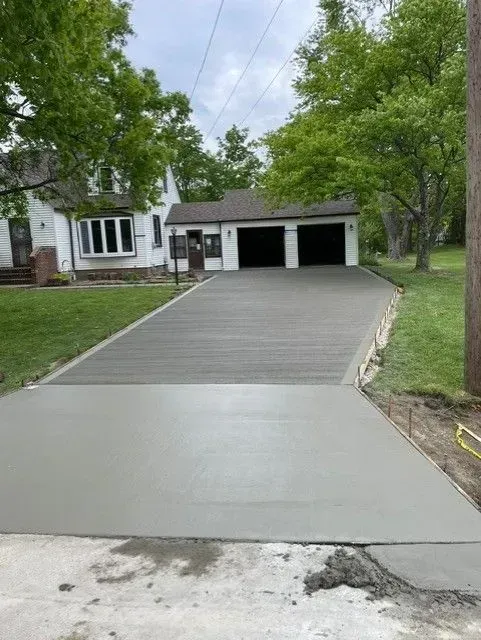 Freshly poured concrete driveway leading to a house with a two-car garage. Overcast sky.