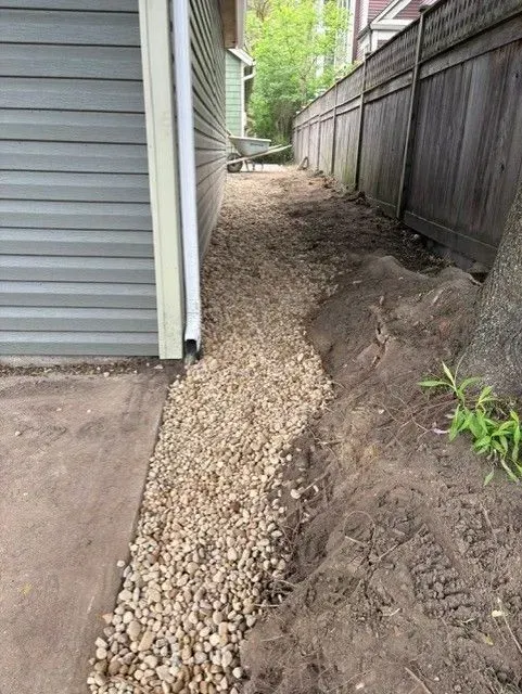 Gravel path alongside a building and fence; dirt area next to gravel.