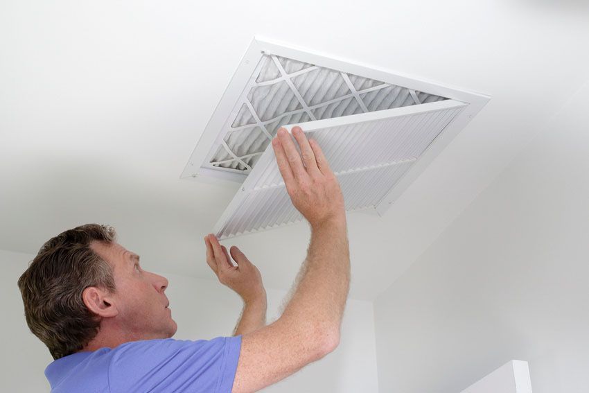 A man is installing a filter on the ceiling of a room.