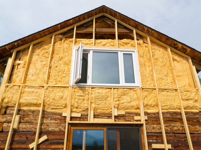 A wooden house is being insulated with spray foam and has a window.