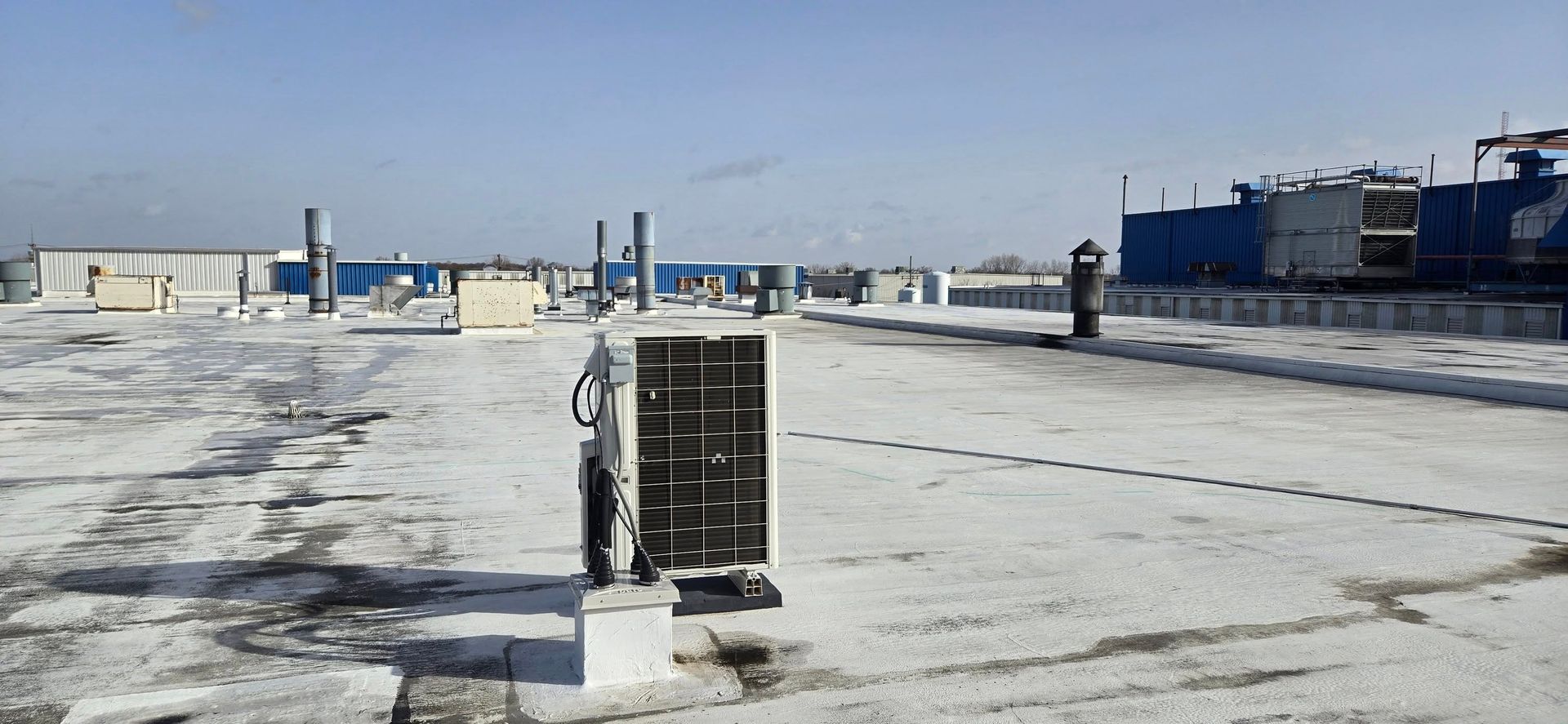 A snowy industrial rooftop with equipment and a solar panel, under a clear blue sky.