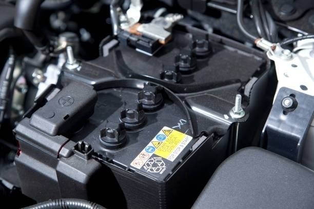 Car battery in engine compartment. Black, rectangular battery with terminals and safety labels.