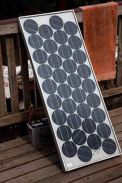 Solar panel leaning against a wooden deck, with a battery and orange towel.