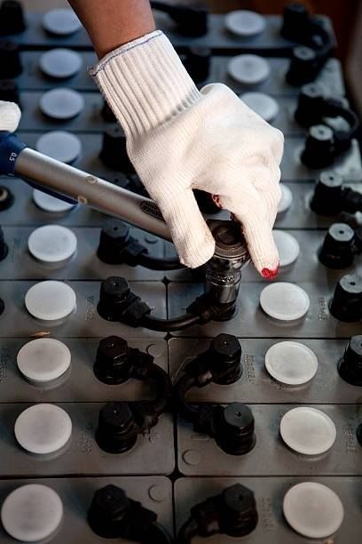 Gloved hand connecting a cable to a battery terminal on a grid of batteries.
