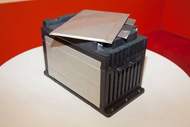 Black and silver battery pack with metal plates on top, sitting on a white surface against a red backdrop.